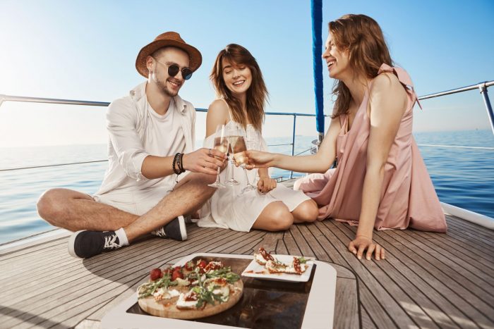 three-trendy-european-friends-sitting-boat-having-lunch-drinking-champagne-expressing-joy-pleasure-every-year-they-book-tickets-warm-countries-winter